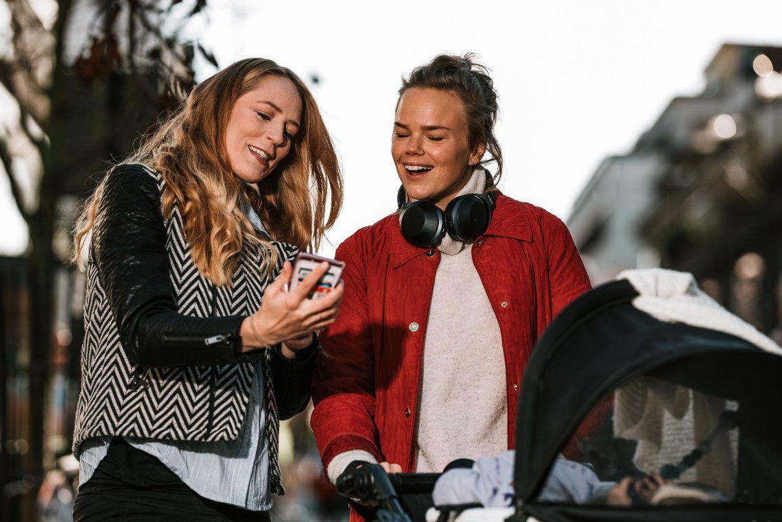 To kvinner ser på mobiltelefon og en barnevogn