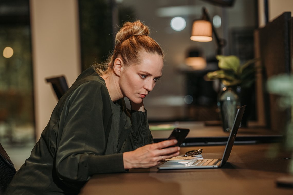 Kvinne som studerer nøye mobil ved pc